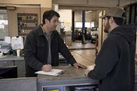 A service advisor talking to a customer at the front counter of a busy American auto repair shop