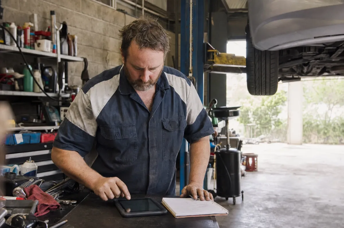 An Australian mechanical workshop owner working out the shop labour rate on a tablet beside a hoisted car