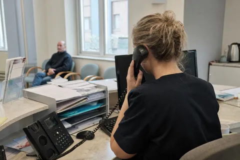 A dental receptionist answering the phone at a busy practice front desk while a patient waits.