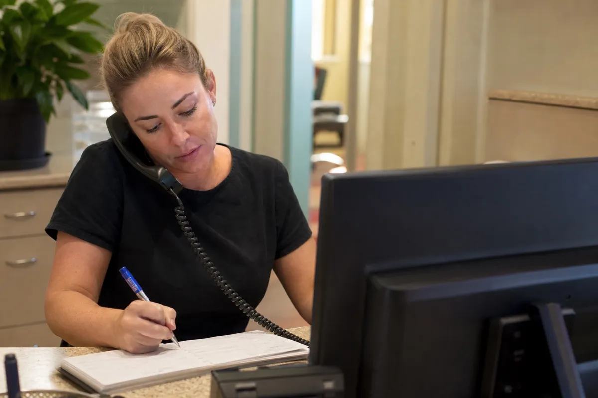 A dental receptionist taking an appointment booking over the phone at the front desk.