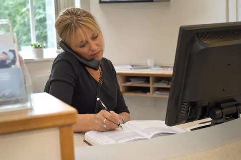 A dental receptionist taking an appointment booking over the phone at the front desk.