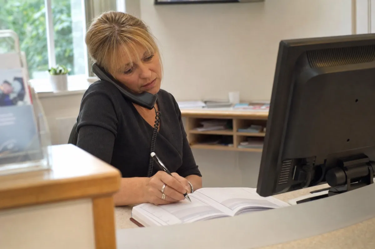 A dental receptionist taking an appointment booking over the phone at the front desk.