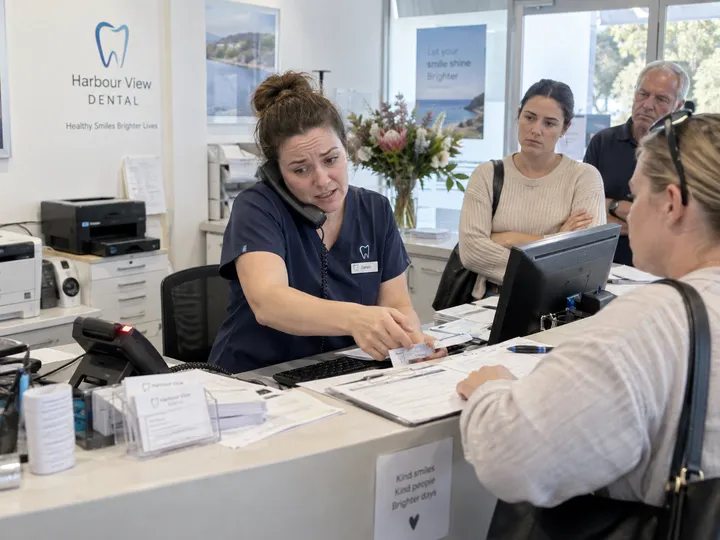 Overwhelmed dental clinic receptionist unable to answer ringing phone while helping patients