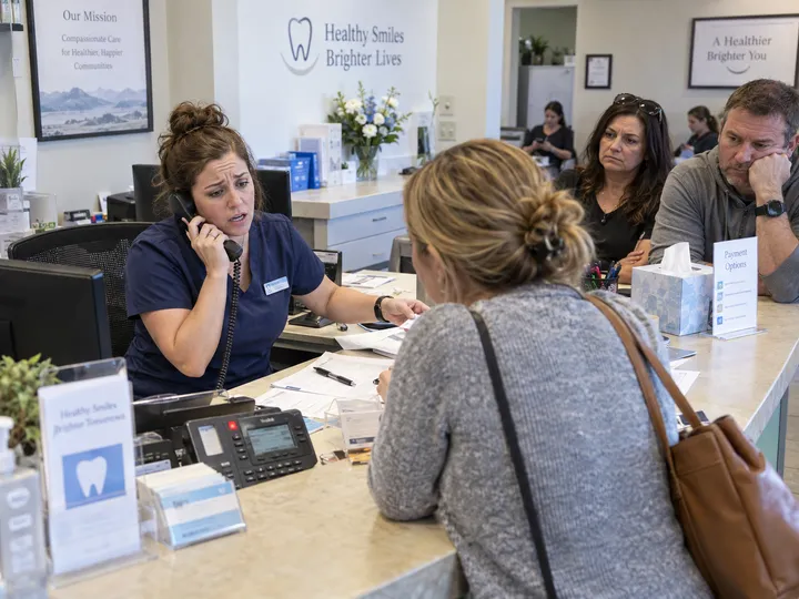 Overwhelmed dental office front desk unable to answer ringing phone while helping patients