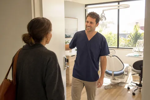 A dentist welcoming a new patient into a bright treatment room.