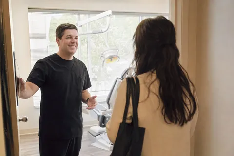 A dentist welcoming a new patient into a bright treatment room.