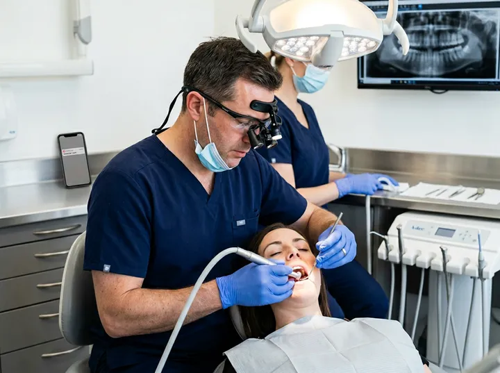 Dentist treating patient while AI receptionist handles incoming phone calls