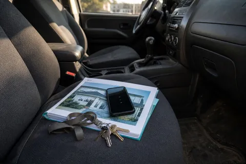 A mobile phone showing missed calls resting on a folder of property details on a car passenger seat