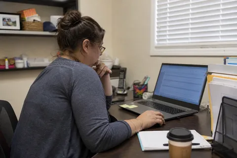A home care scheduler reviewing the visit schedule on a laptop in an agency office
