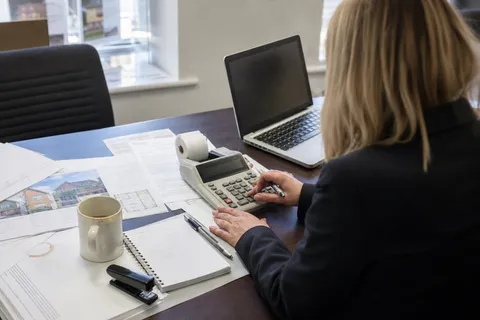 A letting agent working out a property management fee on a desk calculator over rental paperwork and printed property particulars