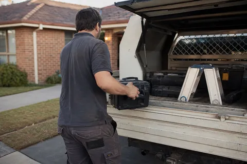 A locksmith loading tools into a sign-written van outside an Australian house at the start of the working day
