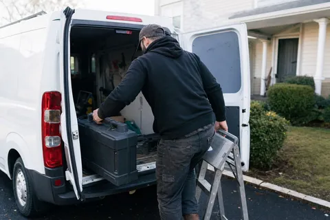 A locksmith loading tools into a sign-written van outside a Canadian house at the start of the working day