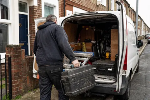 A locksmith loading tools into a sign-written van outside a UK house at the start of the working day