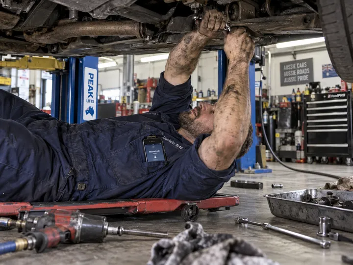 Mechanic working under car while AI handles incoming workshop phone call