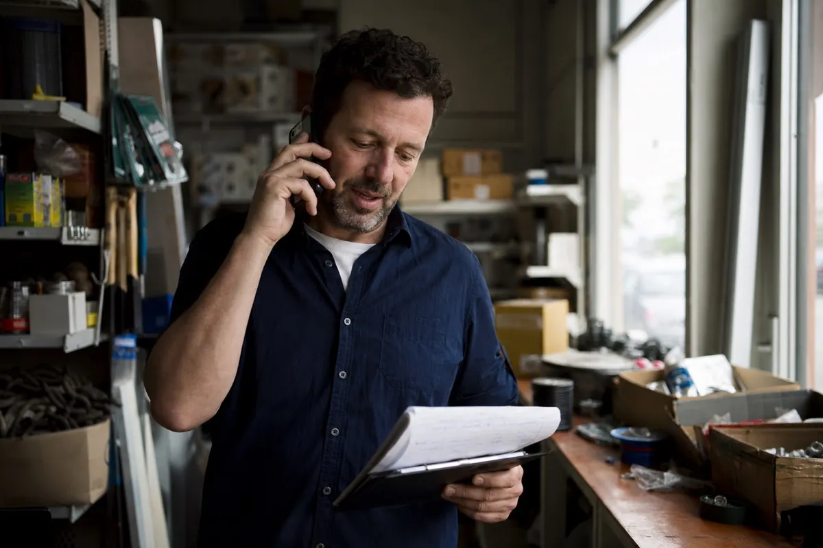 A multi-site business owner on the phone inside one of their shop units, holding a clipboard with notes.
