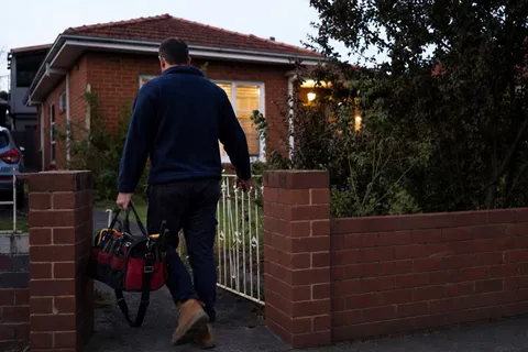 A plumber arriving at a suburban Australian house with a tool bag for an after-hours emergency callout