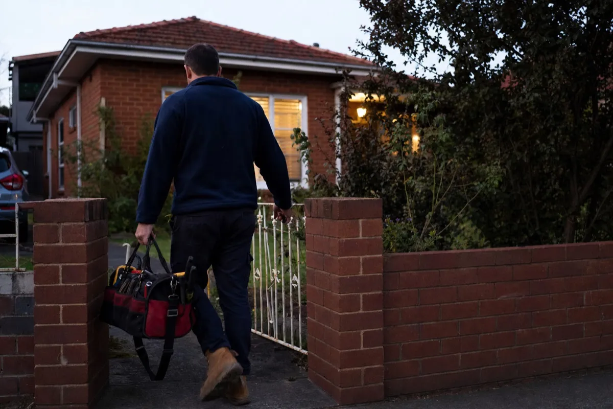 A plumber arriving at a suburban Australian house with a tool bag for an after-hours emergency callout