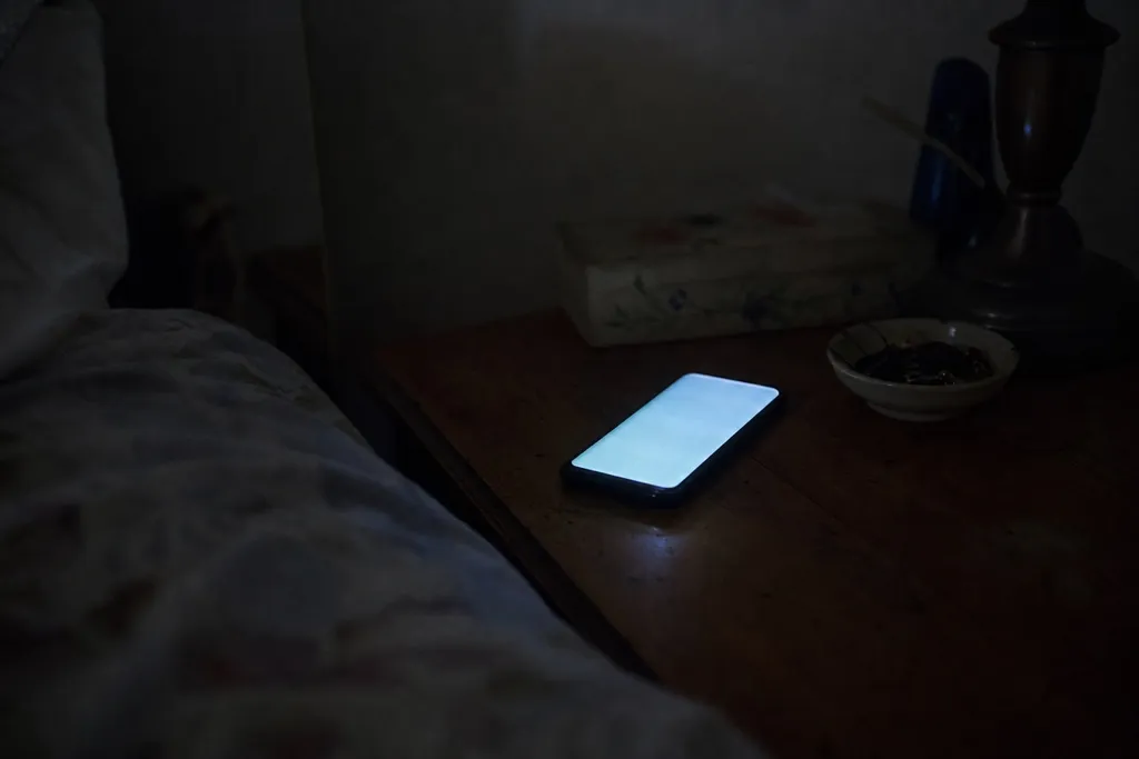 A mobile phone lighting up with a call on a bedside table in a dark room late at night