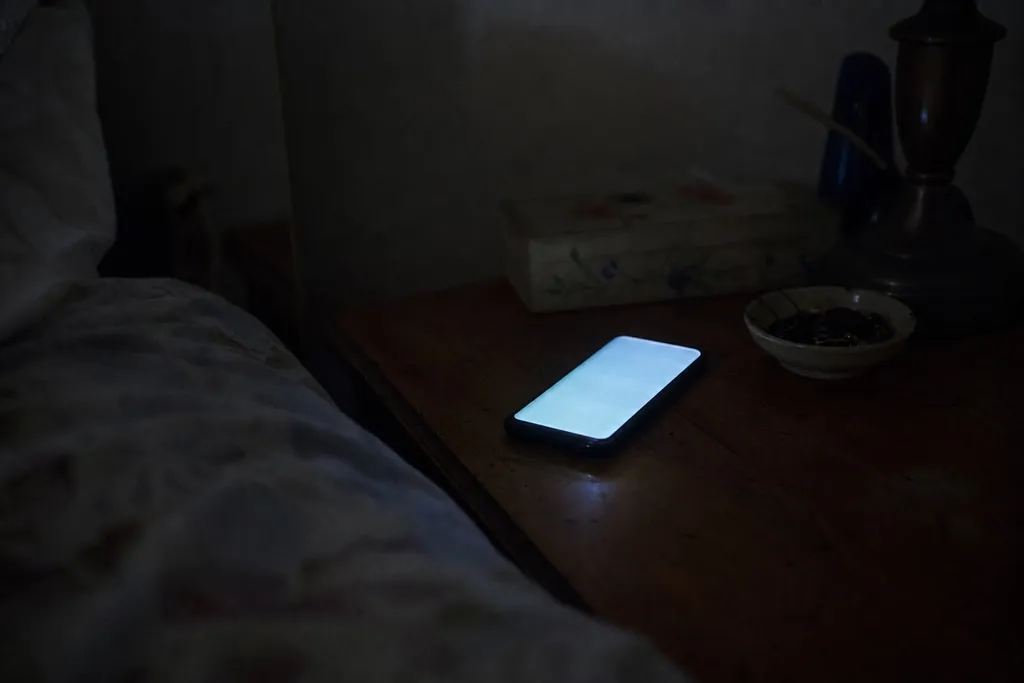 A cell phone lighting up with an incoming call on a nightstand in a dark bedroom late at night