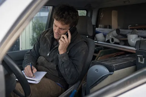 An Australian plumber taking a customer call and writing the job down on a notepad in the back of their ute