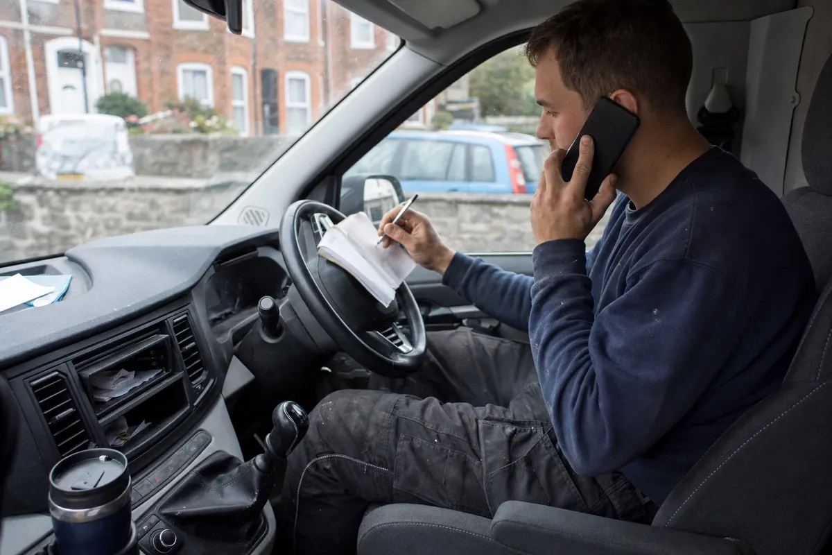 A plumber taking a customer call and writing the job down on a notepad in their work van