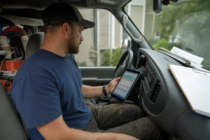 A plumber checking a field-service app on a tablet in the cab of their work truck
