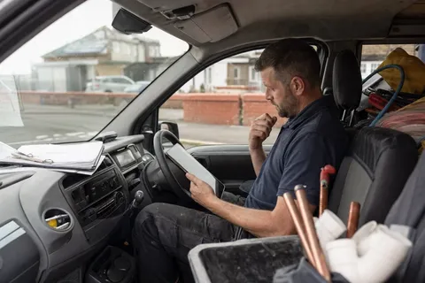 A plumber checking a job-management app on a tablet in the front of their work van