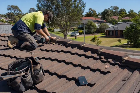 A roofer working on a residential roof while their phone rings unanswered beside their tool bag.