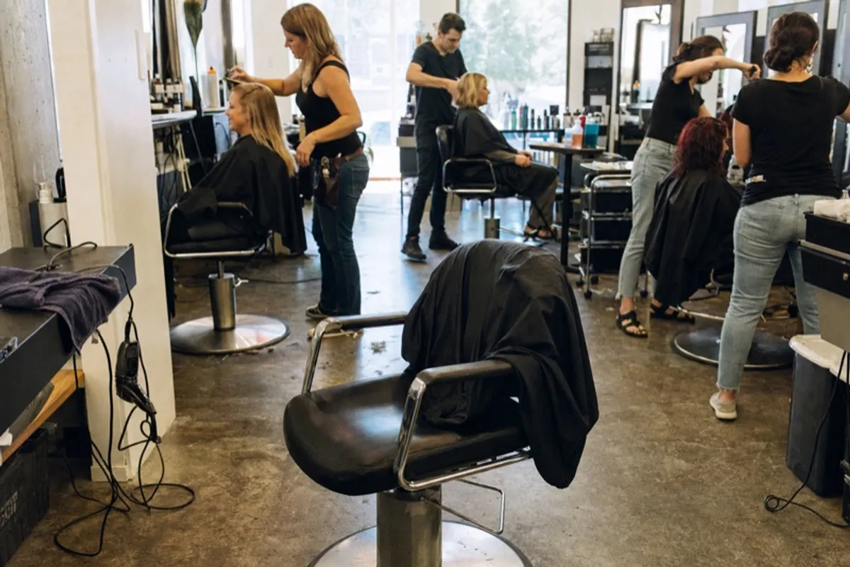 An empty styling chair in a busy American salon while stylists work the other stations