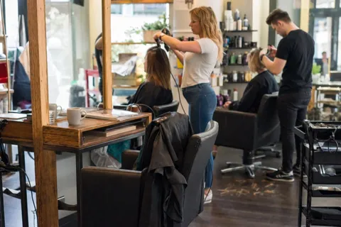 An empty styling chair in a busy salon while stylists work the other stations