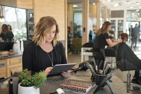 A salon owner checking the day appointments on a booking app at the front desk between clients
