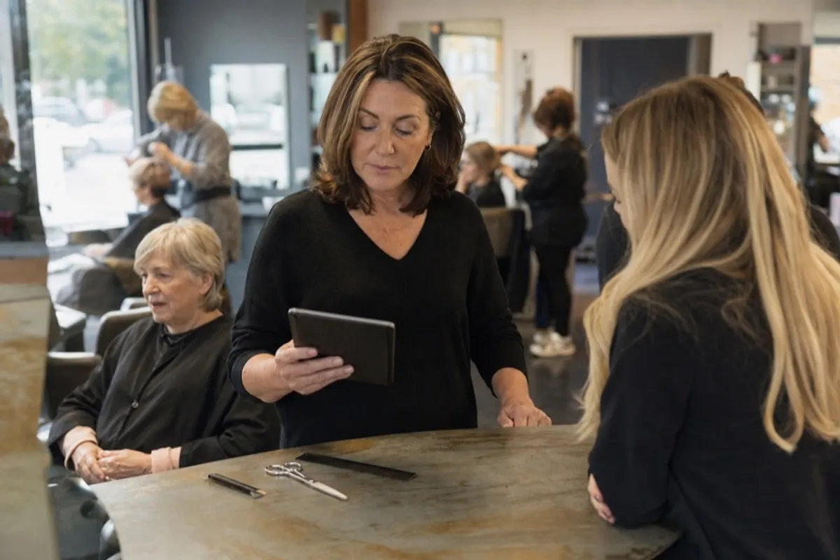 A salon owner checking the day appointments on a booking app at the front desk between clients
