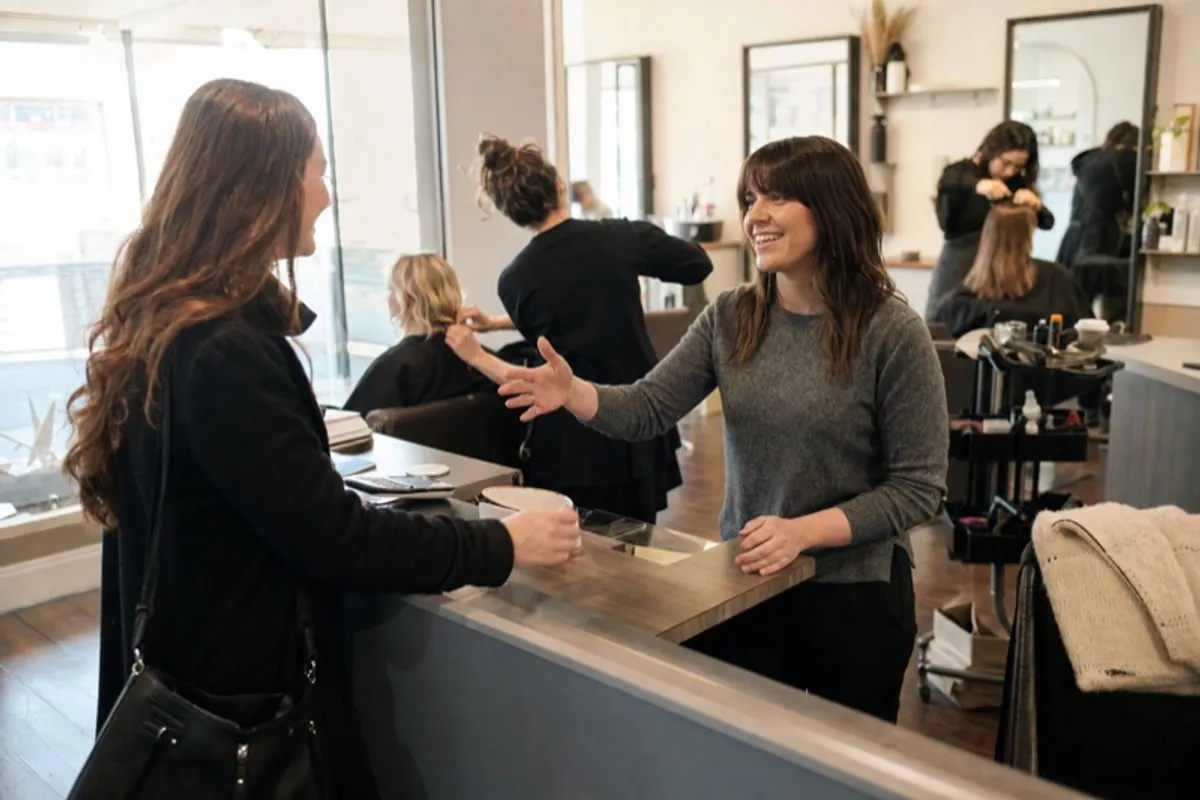 A salon stylist welcoming a new client at the front desk of a busy Irish hair salon
