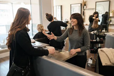 A salon stylist welcoming a new client at the front desk of a busy Irish hair salon
