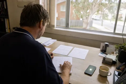 A small business owner at a desk comparing two printed answering service quotes side by side while a mobile lights up with an incoming call, weighing an AI receptionist against a human answering service.