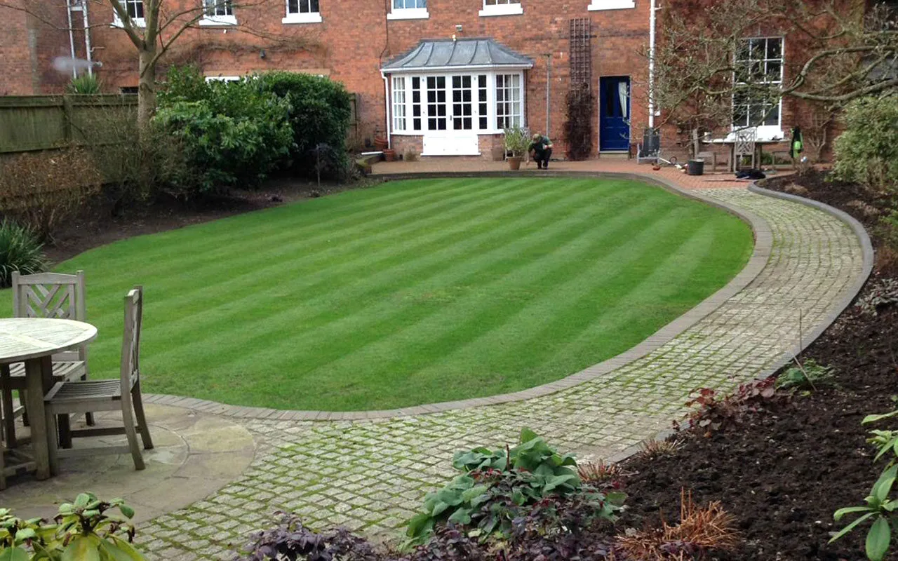 A striped oval lawn in front of a period house, kept by Green Gardeners
