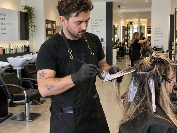Hairstylist applying colour while AI handles incoming booking call