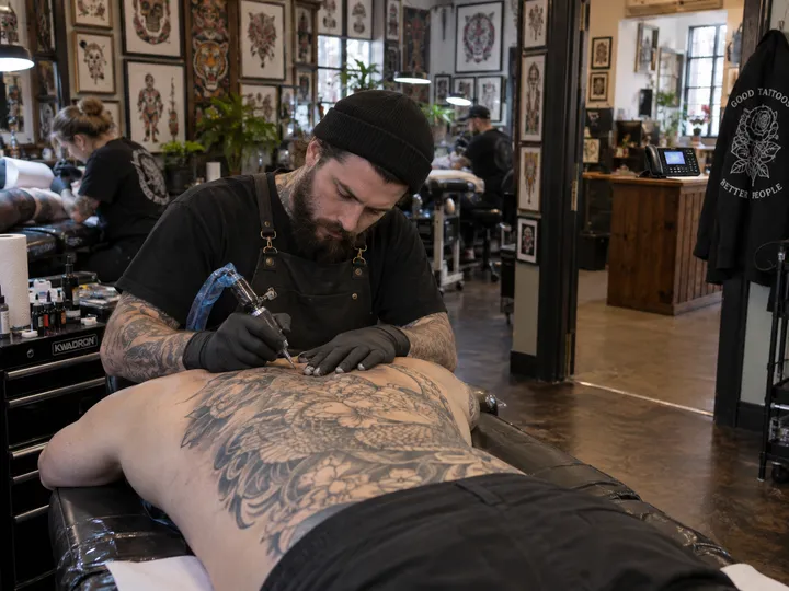Tattoo artist mid-session while AI handles studio phone calls
