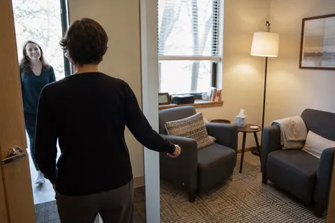 A therapist welcoming a client into a warm consulting room.